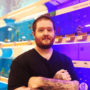 wesley oaks founder of betta fish bay standing in front of a wall of aquariums filled with fish
